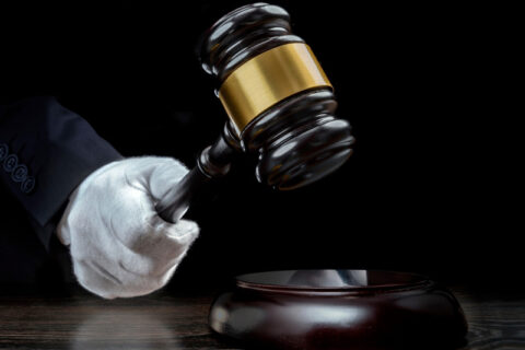 White‑gloved hand holding a gavel above a wooden sound block against a dark background.