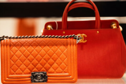 Orange quilted handbag with chain strap displayed in front of a red structured handbag.