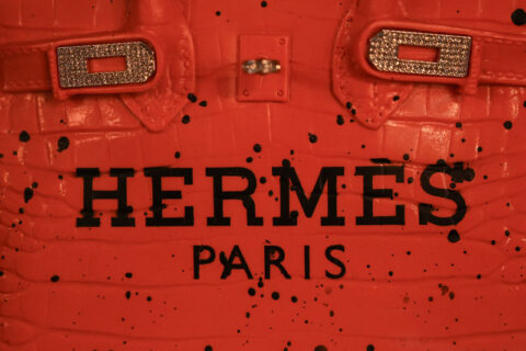 Close-up of a red textured handbag with the text 'HERMES PARIS' and embellished metal hardware.